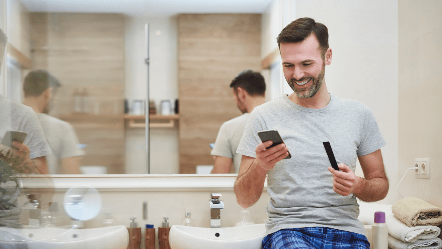 man looking at his phone while holding a Vivoo urine strip